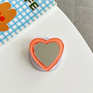 Detail shot of heart-shaped phone grip with orange frame and integrated mirror on back