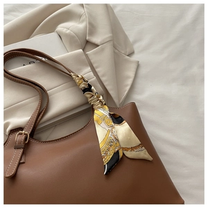 Detailed view of a brown leather tote bag with a silk scarf tied to the strap