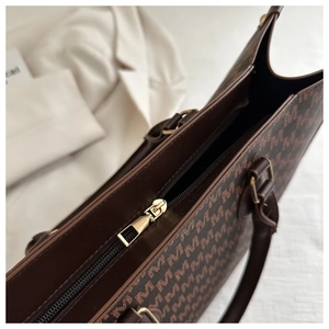 Detailed close-up of brown monogram tote bag with gold metal zipper and handle texture
