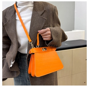 Detalle de un bolso naranja con relieve de cocodrilo y cierre de giro dorado