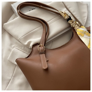 Detail of a brown leather hobo bag with adjustable gold buckles and decorative silk scarf