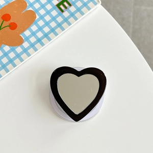 Close-up of black heart-shaped phone grip with built-in mirror on a white desk