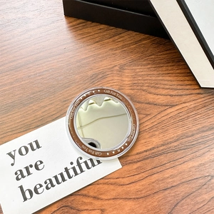 Detail of round magnetic makeup mirror with Gift For You print on dark wood desk