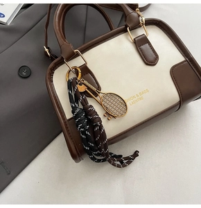 Detail of two-tone crossbody bag with gold tennis racket charm and brand logo