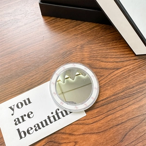 Macro shot of circular makeup mirror with pink bow pattern on a warm wooden surface