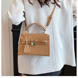 Brown textured leather handbag with metallic lock shown on white blazer outfit
