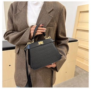 Details einer schwarzen Handtasche mit Krokodilmuster und Goldverschluss auf Wollsakko