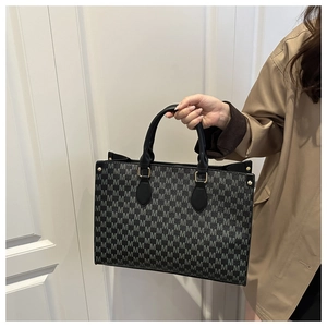 Macro detail of black tote bag with gray M pattern and golden metal buckles