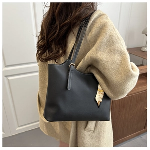 Detail of black leather tote bag with white stitching and yellow scarf on a long coat