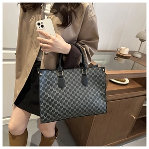 Detailed close-up of large black tote bag featuring classic grey M-letter print and gold hardware
