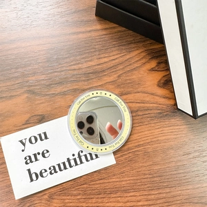 Close-up of a circular portable makeup mirror with Gift For You print on a wooden desk