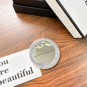 Close-up of circular purple cosmetic mirror with 'Gift For You' text on a wooden desk