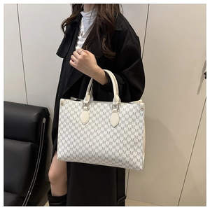 Chic light gray monogram tote bag with leather handles shown in a modern interior setting