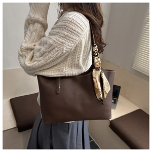 Detail of dark brown leather tote bag featuring a decorative vintage scarf on handle