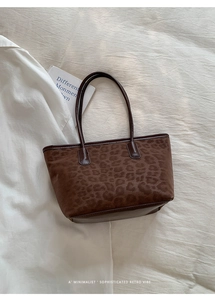 Detail of leopard print tote bag with brown leather handles on white textured background