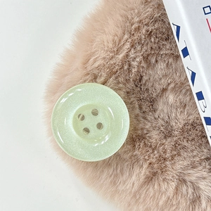Close-up of a pale green glitter button phone grip on a brown plush surface