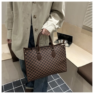Close-up of brown tote bag with all-over M pattern and premium leather handles