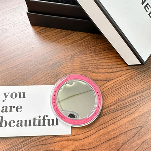 Close-up of a round pink portable makeup mirror with star patterns on a wooden surface