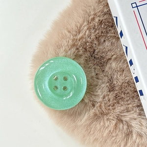 Detailed macro view of a mint green glitter resin button with four-hole design on fur