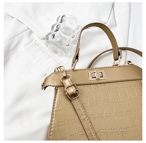 Détail du sac à main doré avec motif crocodile, fermoir rotatif et bandoulière chic