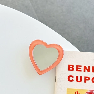Close-up of heart-shaped coral orange folding phone mirror grip on a white surface