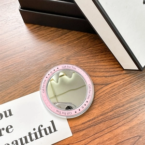 Close-up of a pink round portable makeup mirror with Gift For You text on dark wood