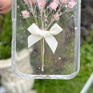 Detail of transparent iPhone case with dried flowers, white bow, and silver glitters