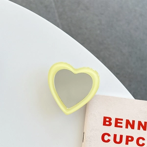 Close-up of a heart-shaped yellow phone grip and makeup mirror on a modern desk