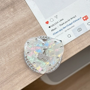 Detail der herzförmigen Handyhalterung mit Perlmutt-Finish und Strass-Kirsch-Dekor