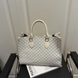 Minimalist beige tote bag with M letter prints and gold hardware on a leather chair