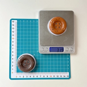 Detail of 31.9g button-shaped ink splash phone grips on a digital scale for size check
