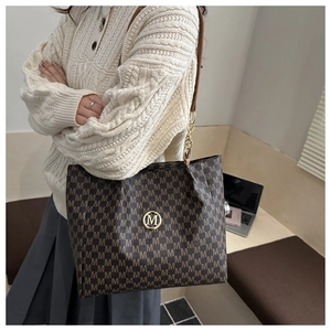 Detail of dark brown tote bag featuring luxury M-letter print and gold metal logo