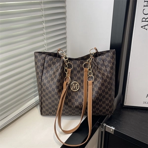 Grand sac cabas marron avec imprimé M et chaîne dorée sur un rebord de fenêtre