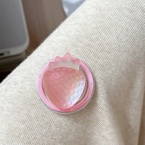 Close-up of a pink resin strawberry phone socket grip on beige knit fabric