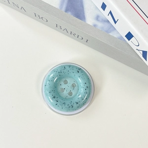 Detail of mint green button-style phone grip with artistic black ink splash texture