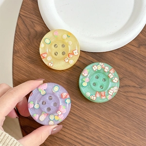 Close-up of glittery resin fruit-themed phone grips on a dark wooden table background