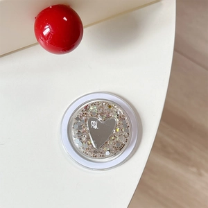 Detail of round phone grip with silver glitter sequins and mirror heart featuring mi ne text