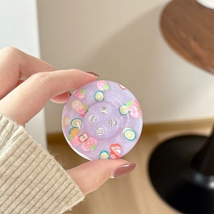 Close-up of a purple glitter button phone grip with colorful fruit patterns being held