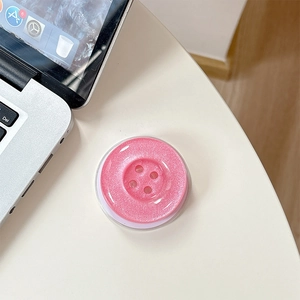 Macro shot of pink glitter button phone grip on white desk showing sparkly texture