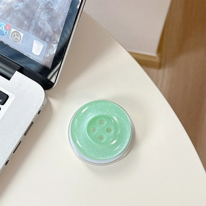 Glittering light green button phone grip stand on desk with laptop background