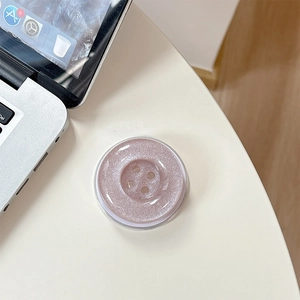 Close-up of a pink glittery button-style folding phone socket holder on a white desk