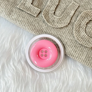 Makro-Detail einer rosa Knopf-Handyhalterung auf weißem Plüsch mit Stricktextur