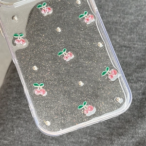 Macro view of clear phone case featuring pink rhinestone cherries and glittery silver texture