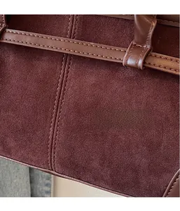 Close-up of the burgundy suede fabric texture and contrast stitching on the shoulder bag