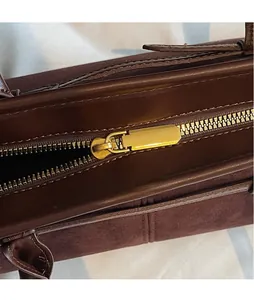 Detailed close-up of smooth brown leather handbag featuring a premium gold metal zipper puller