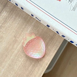 Macro view of a 3D pink strawberry phone grip with iridescent finish on wooden surface