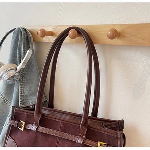 Detail of vintage brown tote bag texture and gold buckle hanging on a wooden hook