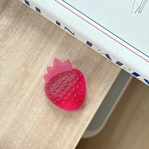 Detail of a bright red strawberry-shaped phone grip on a natural wood surface
