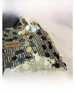 Macro shot of large shiny sequins and the metal brand tag on this shoulder bag