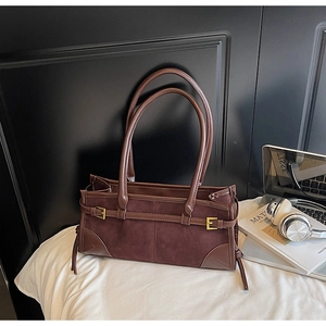 Detail of dark brown faux suede underarm bag featuring decorative straps and gold buckle